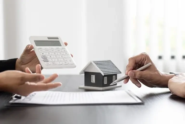 Two individuals holding a calculator and a house model, discussing finances and real estate investments representing to improve your 5 C's of credit